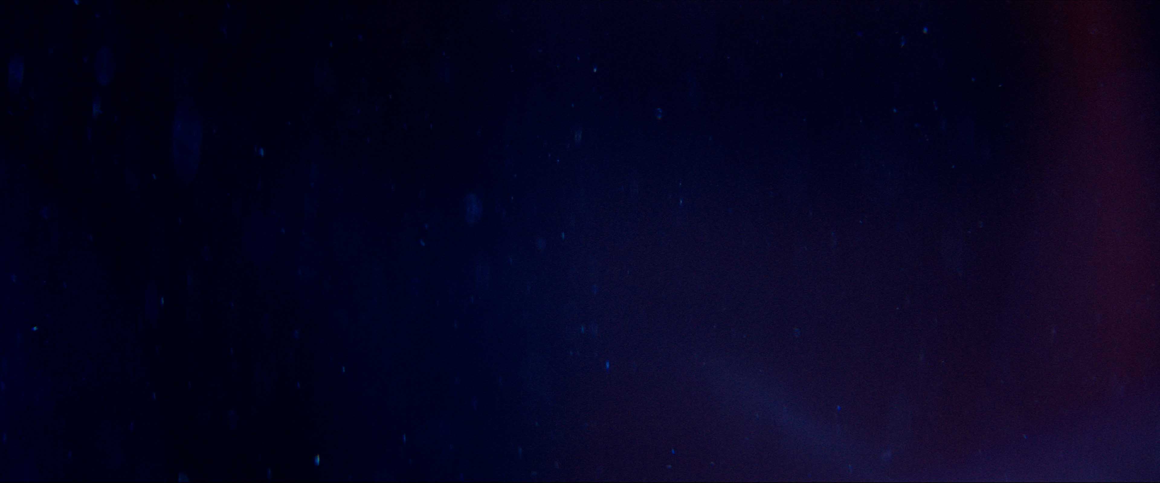 Silhouette of a helmeted racing driver at dusk, mountain skyline faintly visible under violet sky.