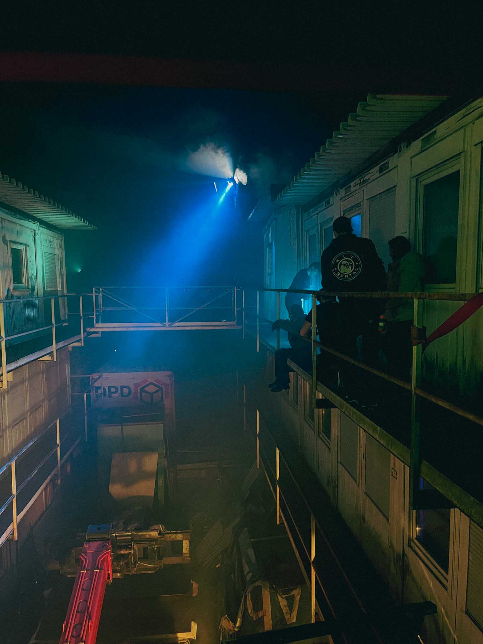 Front-facing Porsche GT3 with headlights on, carving through a chicane at twilight in alpine scenery.