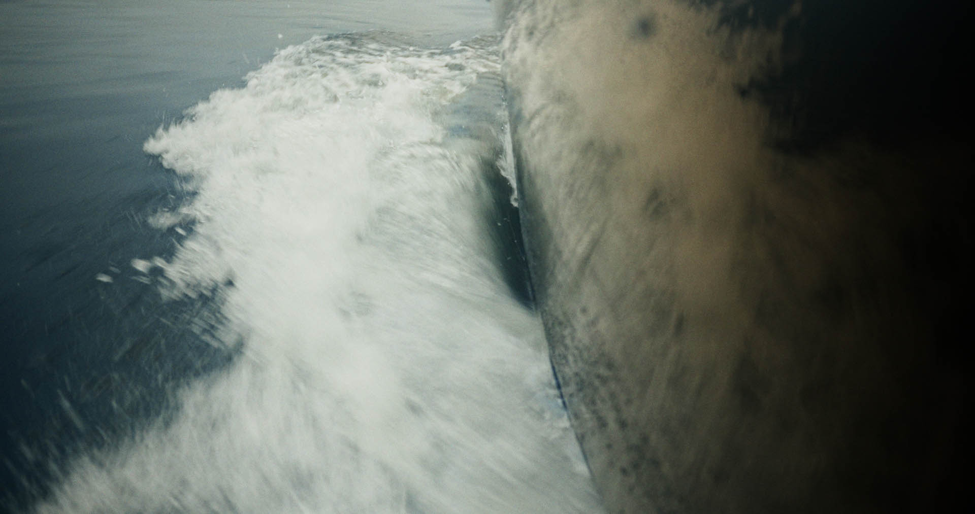 Front-facing Porsche GT3 with headlights on, carving through a chicane at twilight in alpine scenery.