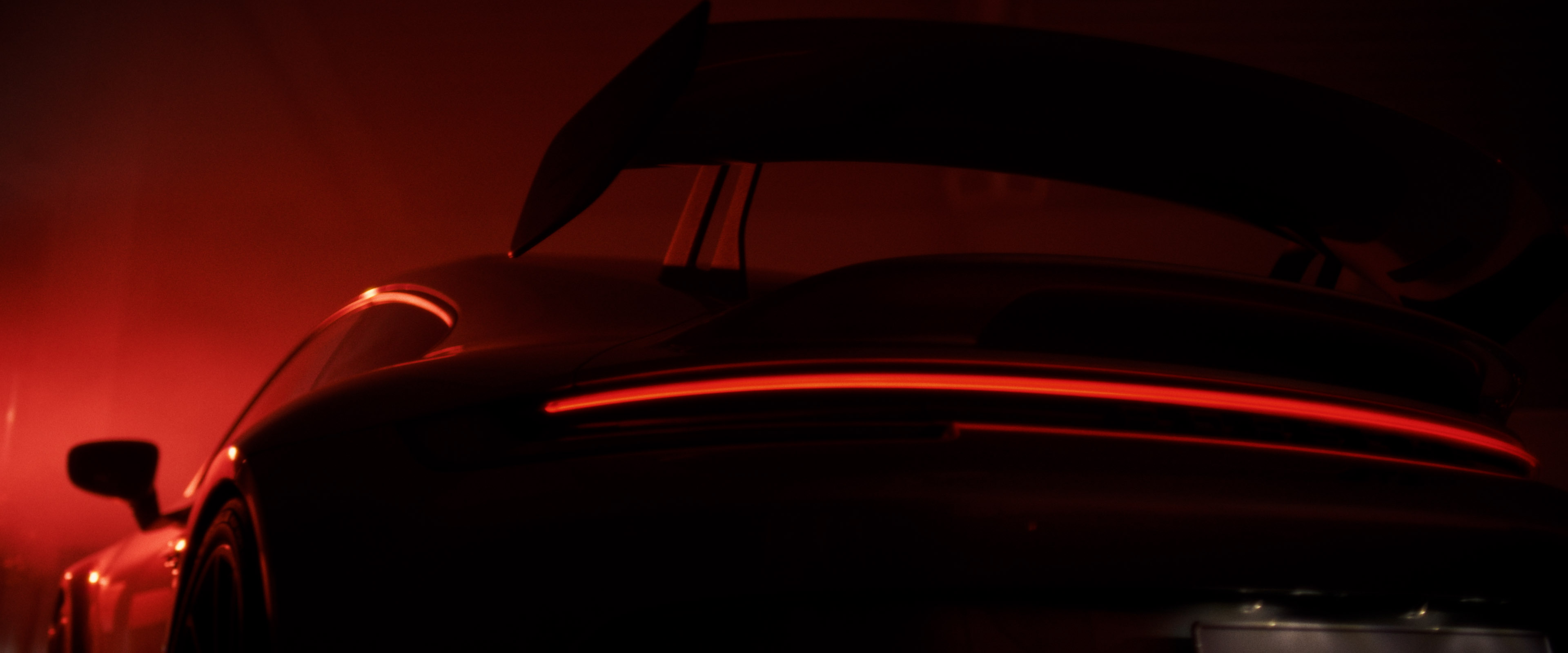 Close-up of a Porsche 911 GT3 rear wing and glowing LED taillight, bathed in deep red tunnel light.