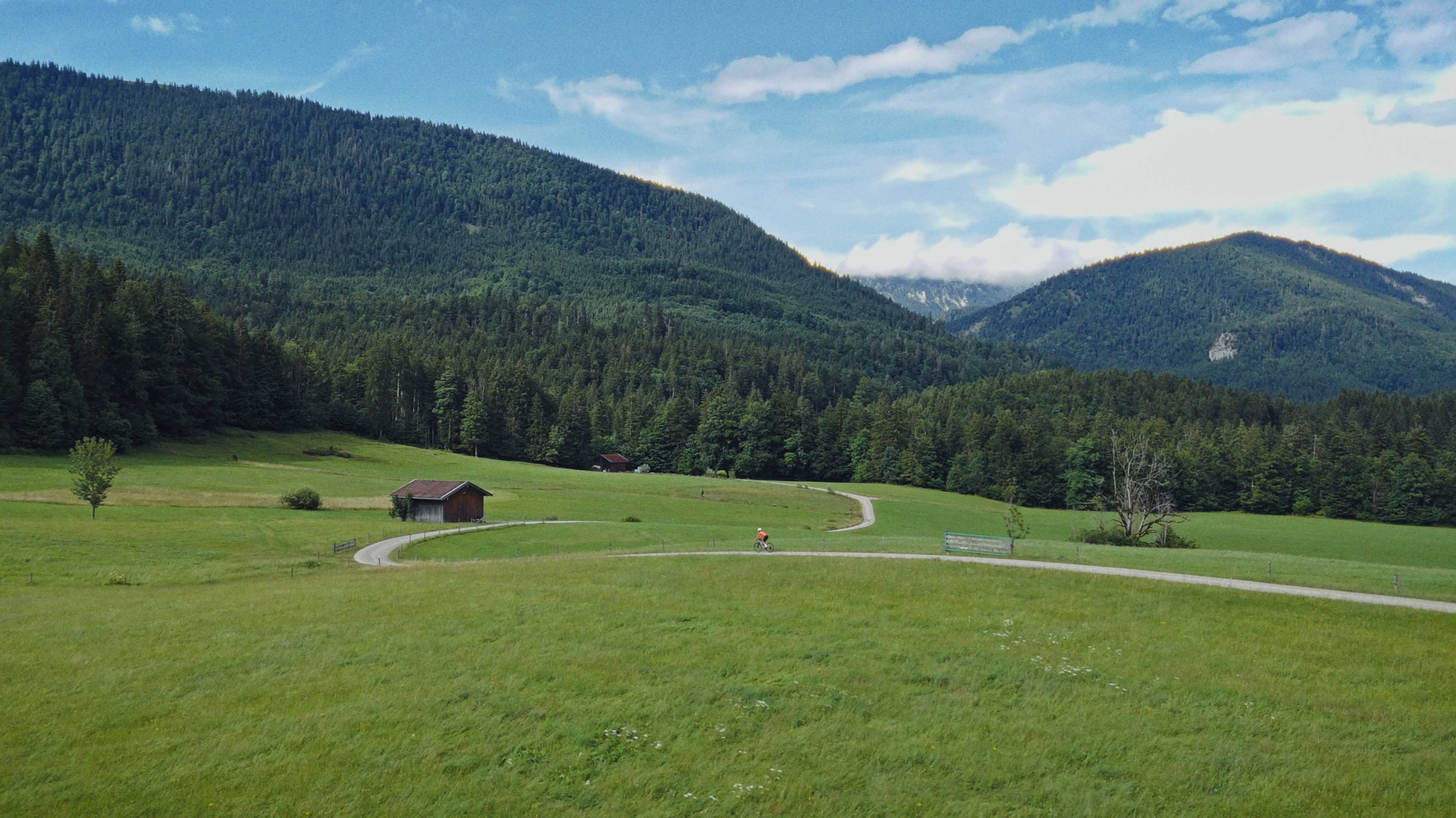 Aerial view of an alpine lakeside road with avalanche gallery; tiny sports car speeds along the shoreline.